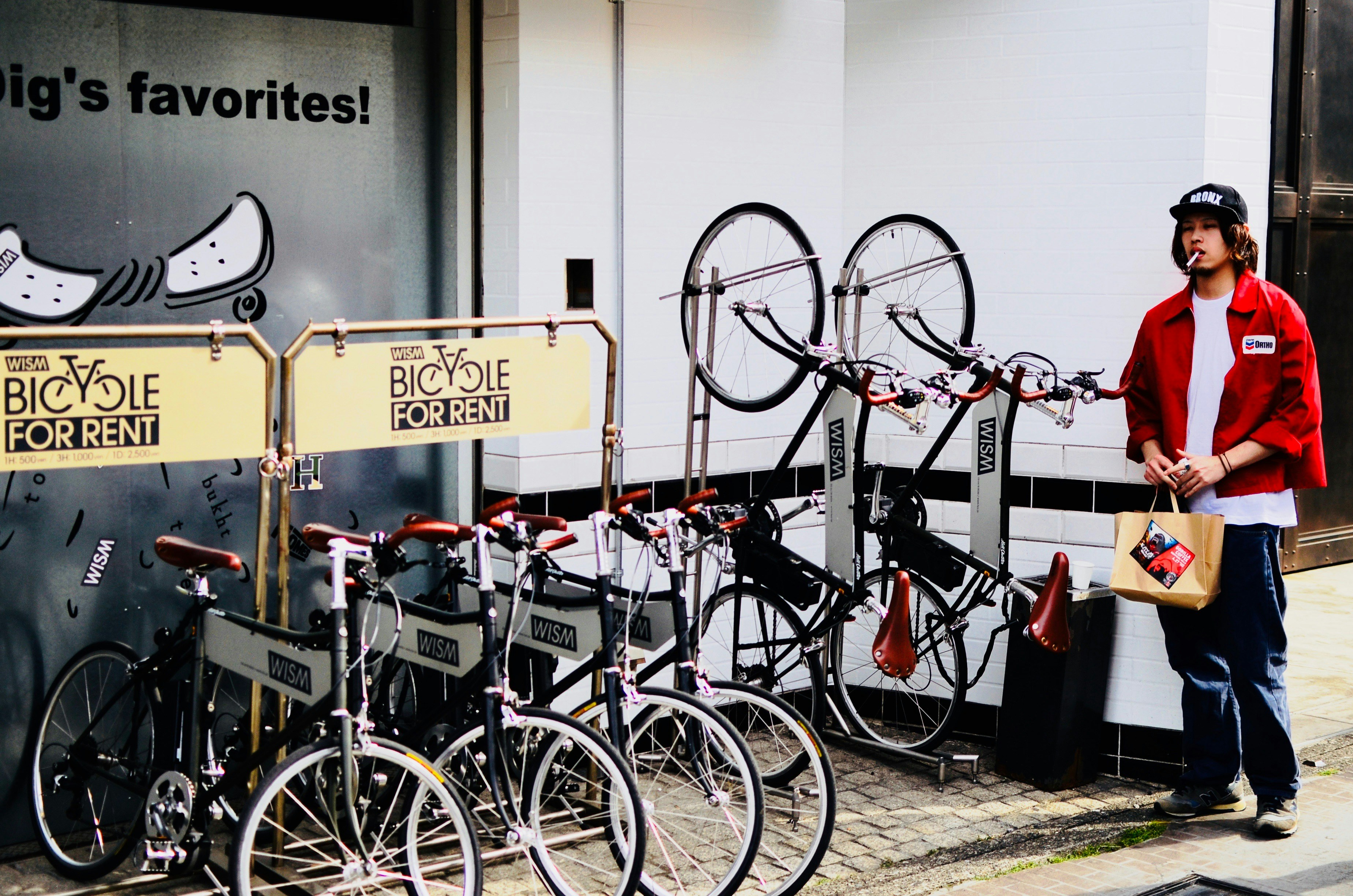 man wearing red button-up shirt walking near bicycle parking space