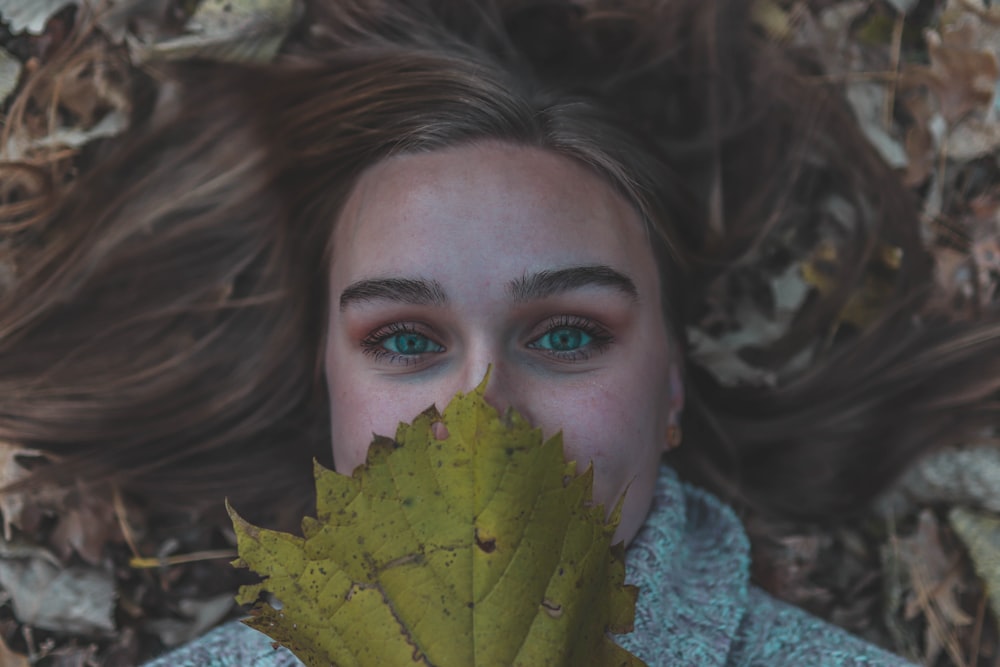 woman lying on dried leaves and holding green leaf