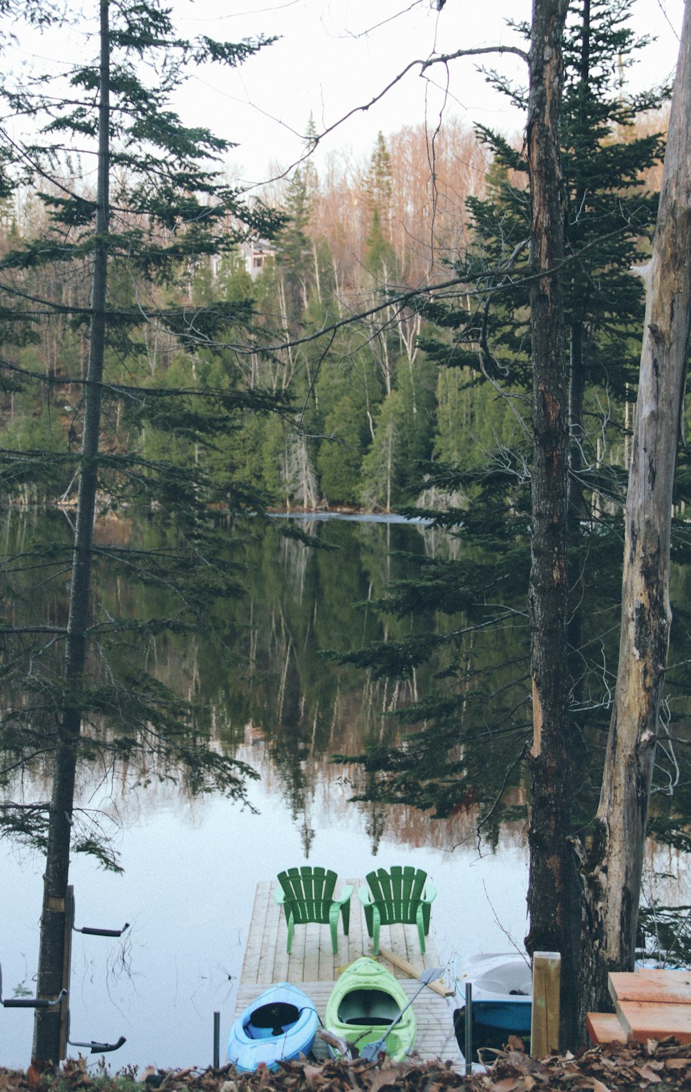 two empty green Adirondack chairs on wooden dock above body of water