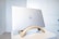 A silver Dell laptop placed on a wooden stand, situated on a white table against a light-colored wall. The scene is minimalistic and clean, with the focus on the sleek design of the laptop and its stand.