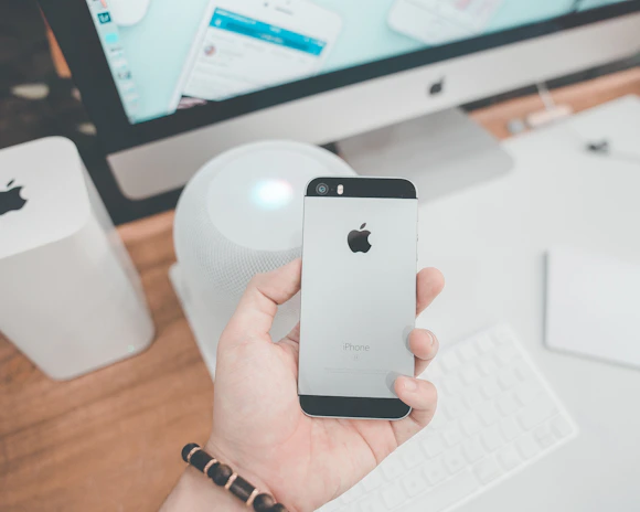 Close-up of hands setting up an iPhone with cables and tech tools on a wooden desk.