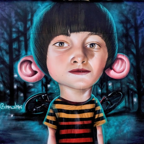 A mural portrays a young child with exaggerated large ears, wearing a striped shirt. The background consists of a dark forest setting, with trees silhouetted against a blue-toned night sky. A bicycle is partially visible behind the child.