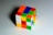 A partially solved Rubik's Cube is positioned on a flat, light-colored surface. Each side of the cube features a grid of smaller squares with different colors, including red, blue, green, yellow, orange, and white.