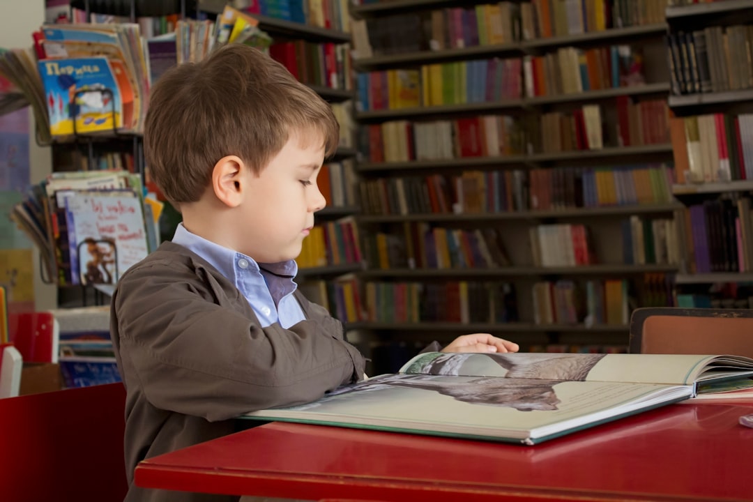 boy sitting near red table reading book,