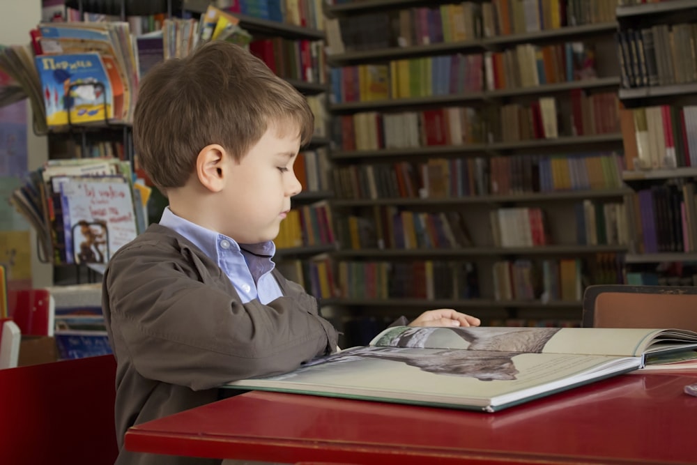 赤いテーブルの近くに座っている男の子が本を読んでいます