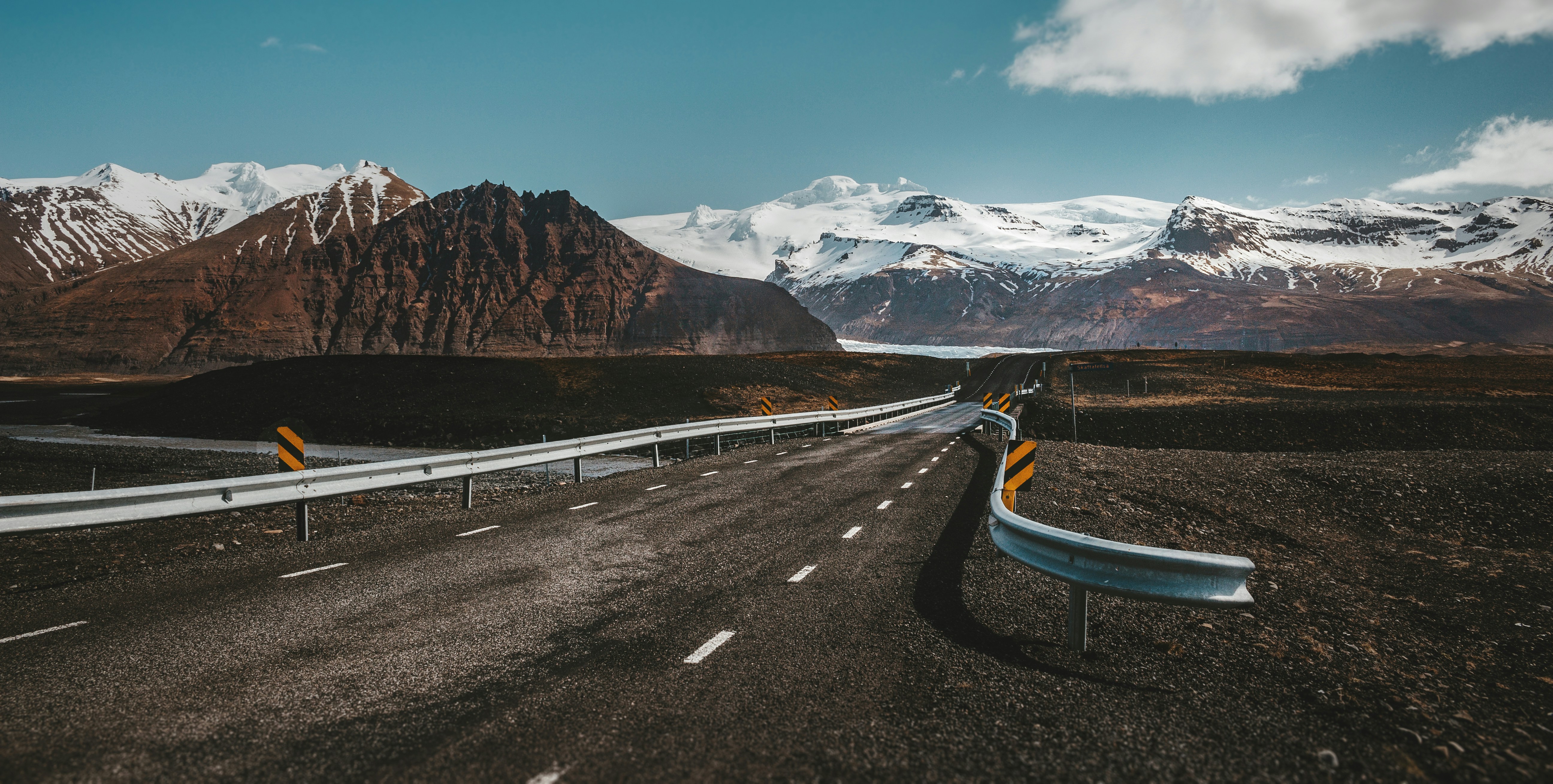 grey and white highway near lake with view of snow-capped mountain