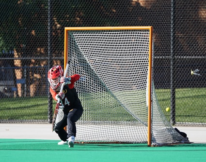 man in red helmet holding stick near goal net