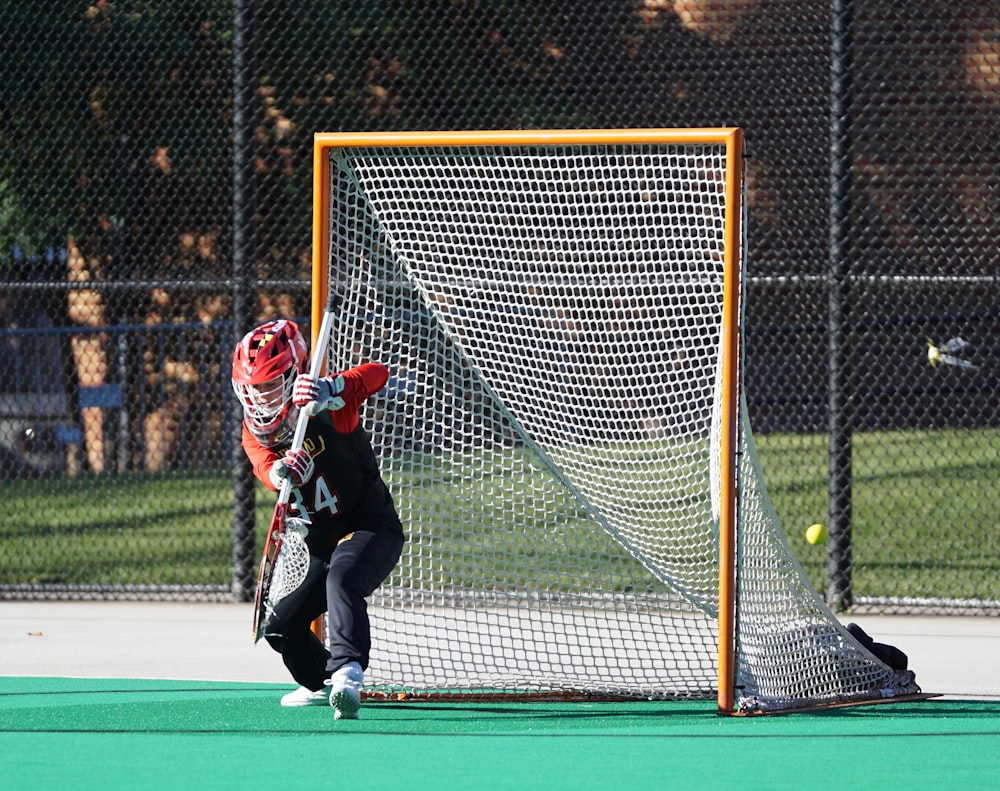 man in red helmet holding stick near goal net