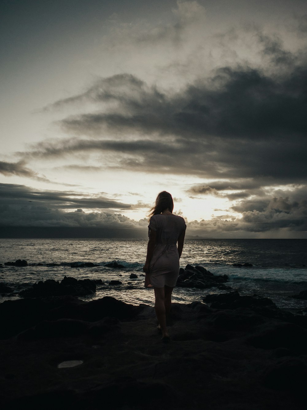 海の波のそばに立つ女性のシルエット写真