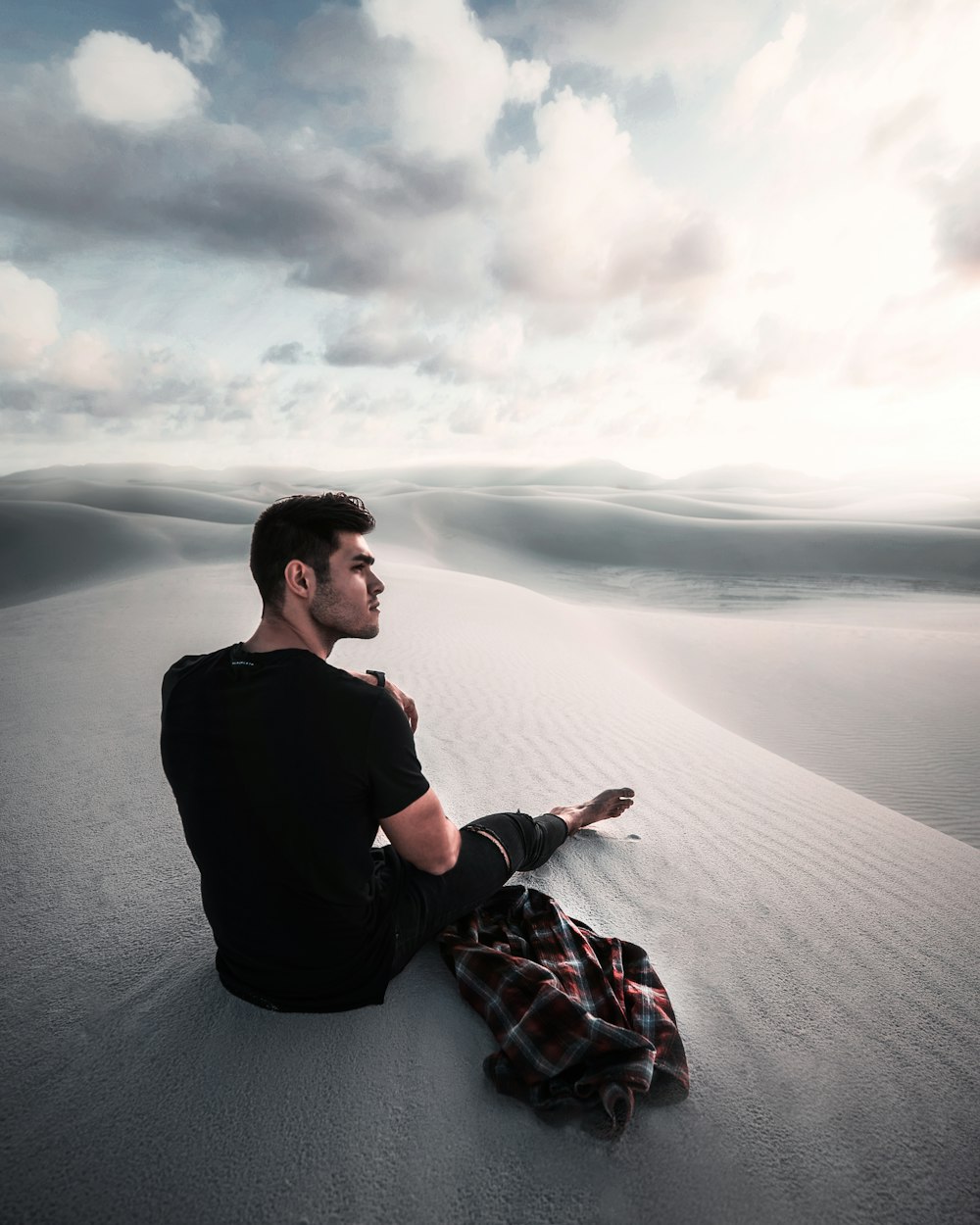Homme assis sur le sable gris sous un ciel nuageux pendant la journée