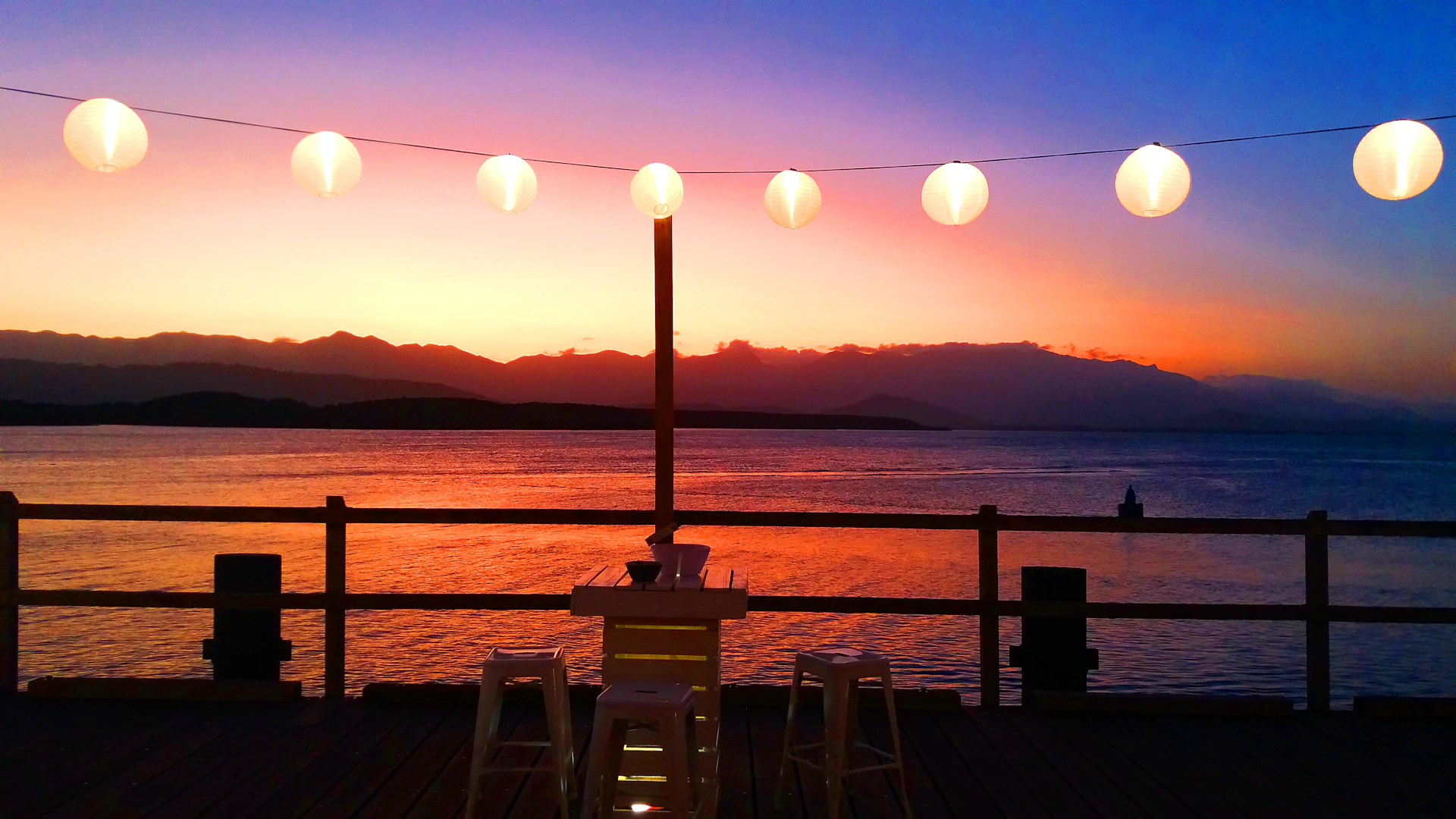 A twilight view from the beachfront deck, with warm string lights glowing and a hammock inviting guests to relax while watching the sunset.