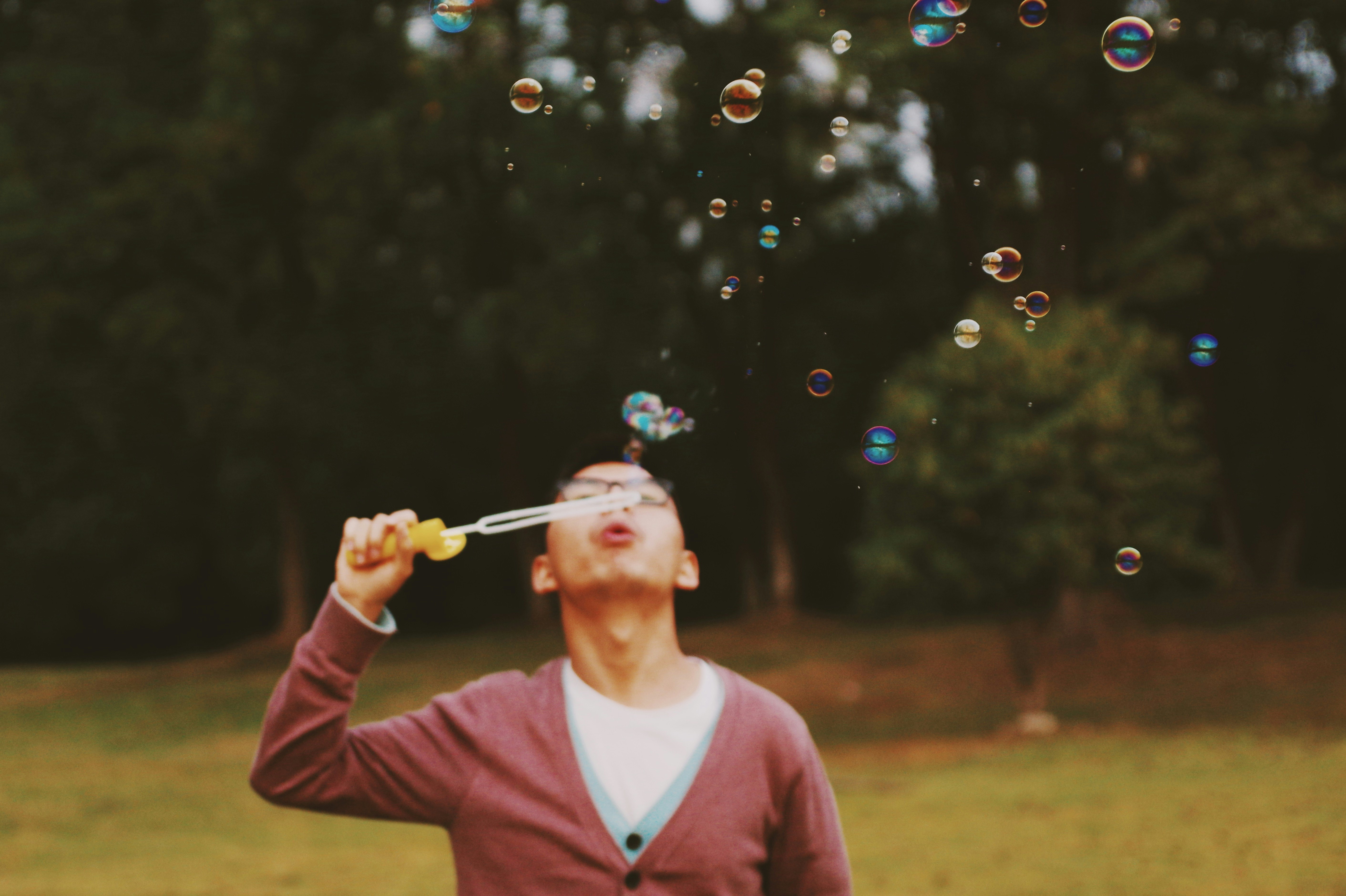 man holding bubble stick near green trees