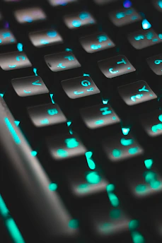 Close-up of hands typing on a charcoal keyboard with a deep teal screen showing AI-driven analytics.