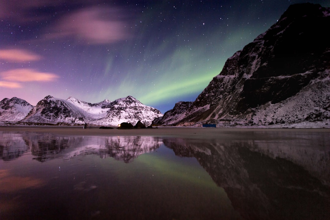 lake beside mountain covered with snow under aurora borealis