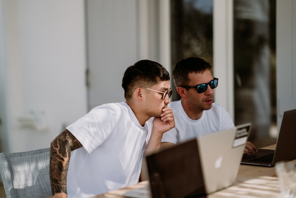 two men sitting on chairs while using laptop computers