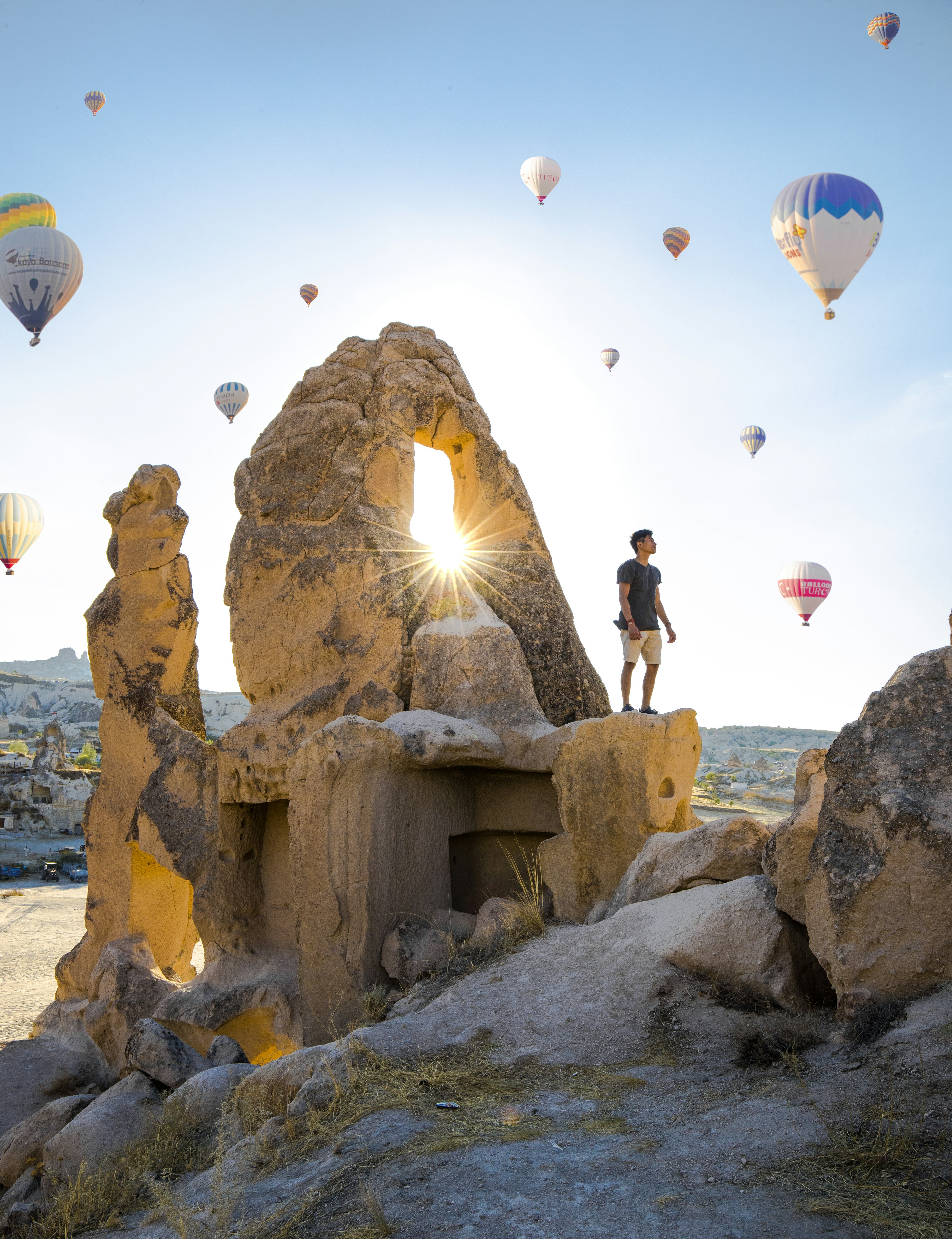 man standing on rocky hill and assorted-colored hit air balloons on skies