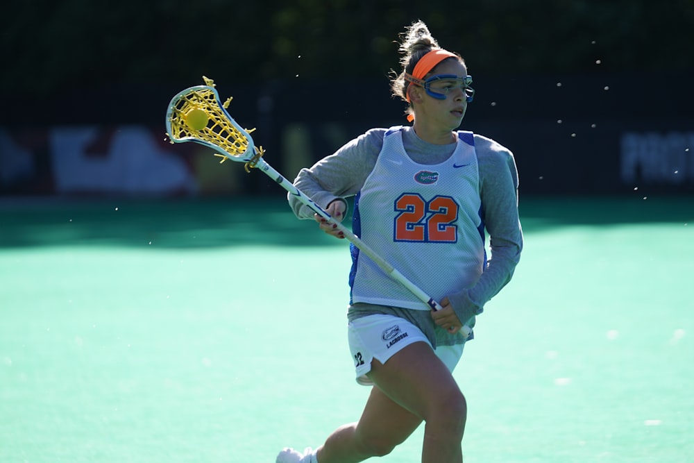 mulher jogadora de lacrosse correndo em campo durante o dia