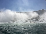 Niagara Falls roaring with mist rising under a bright blue sky.