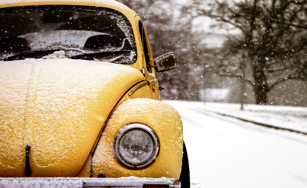 yellow Volkswagen Beetle on road covered by snw