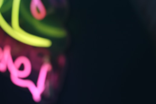 Blurred neon lights create an abstract visual with shades of green and pink set against a dark background.