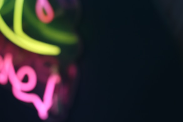 Blurred neon lights create an abstract visual with shades of green and pink set against a dark background.