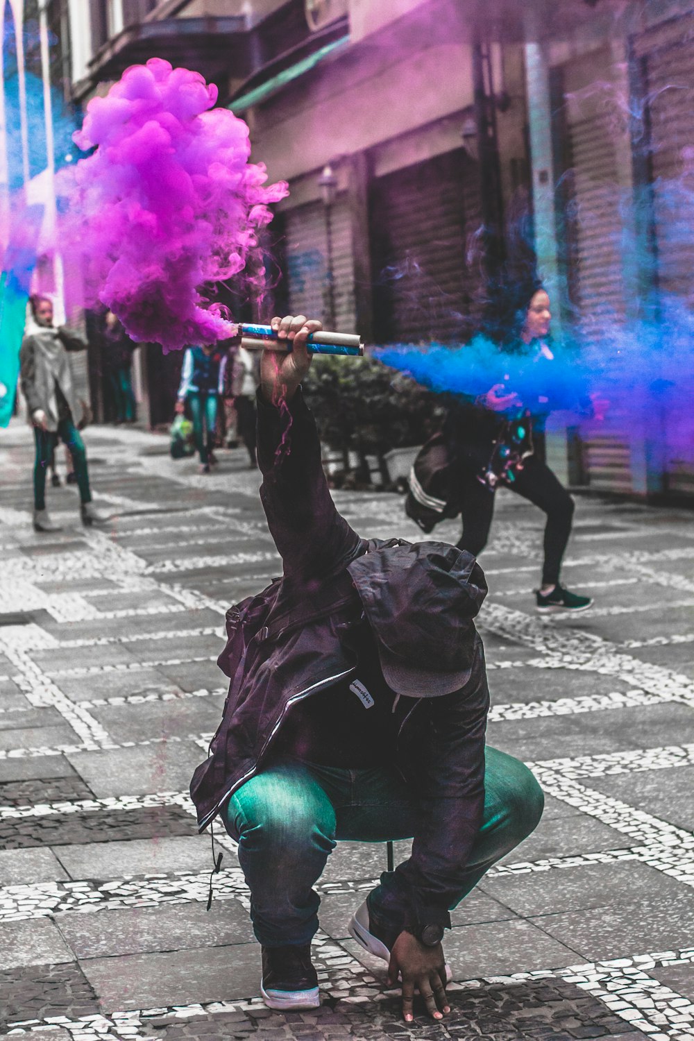 man squatting while holding purple and blue smoke at daytime