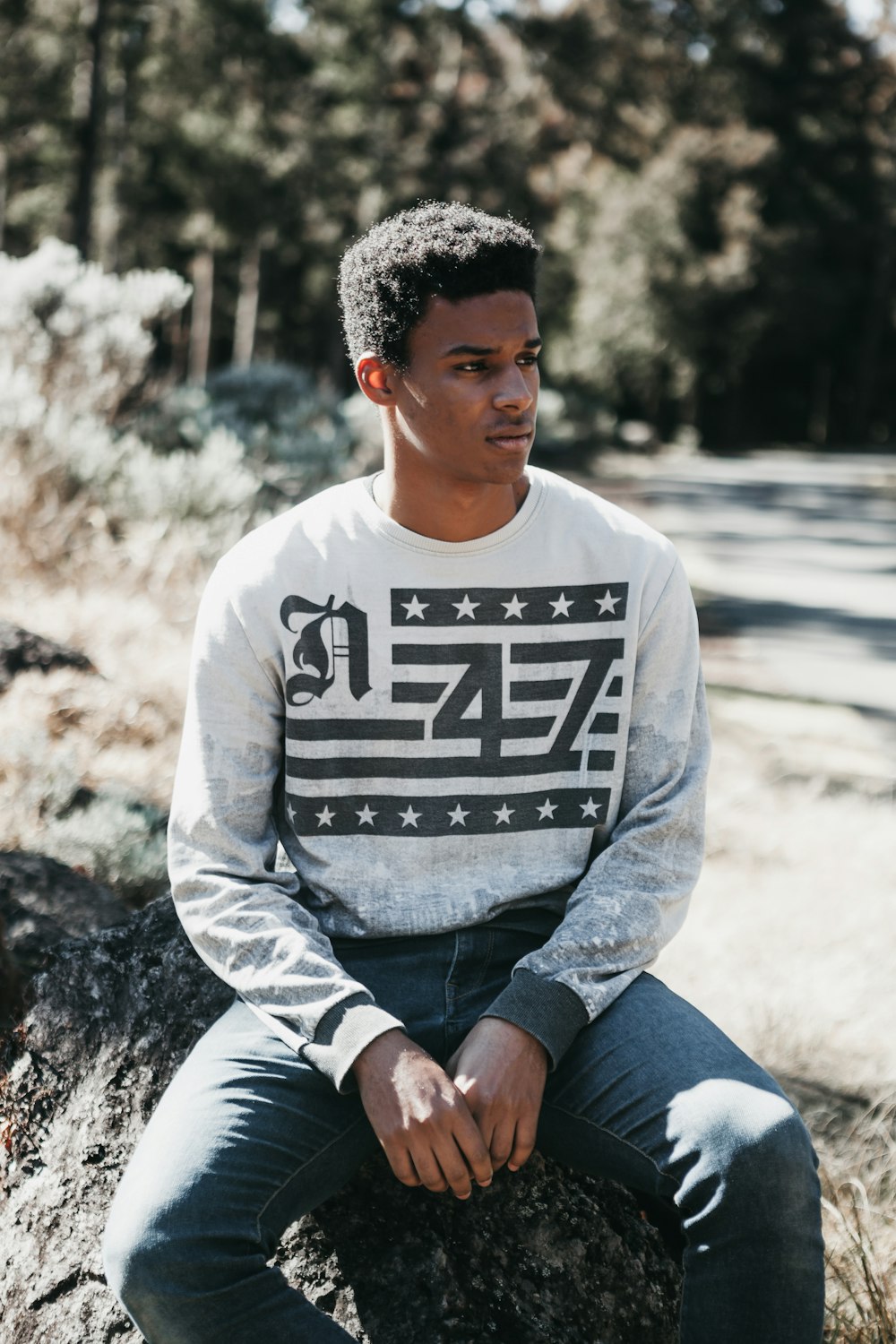 man in gray sweater sits on rock while looking into left