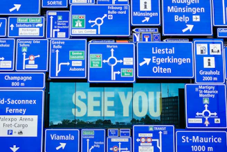 See You displayed on glass window with blue road signage hanging outside the window