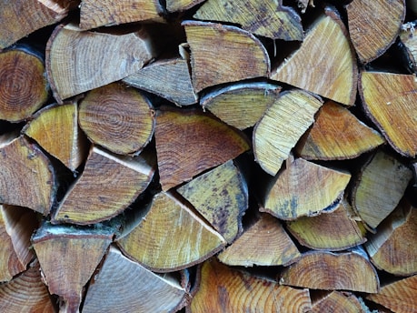A stack of neatly arranged firewood, consisting of cut logs with visible growth rings and natural wood texture. The logs are stacked in a closely packed, organized manner.