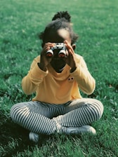 girl sitting on grass field holding binoculars