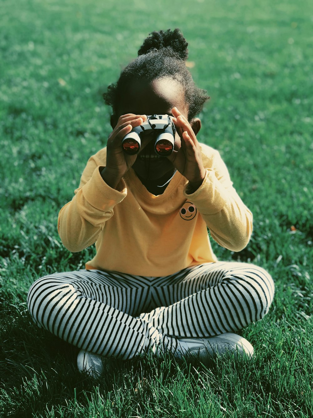 girl sitting on grass field holding binoculars