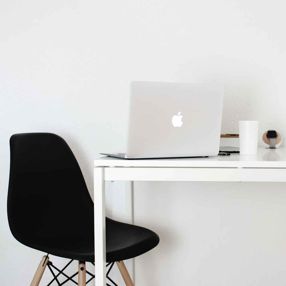 Ein Apple-Laptop, der auf einem Schreibtisch neben einem schwarzen Stuhl sitzt