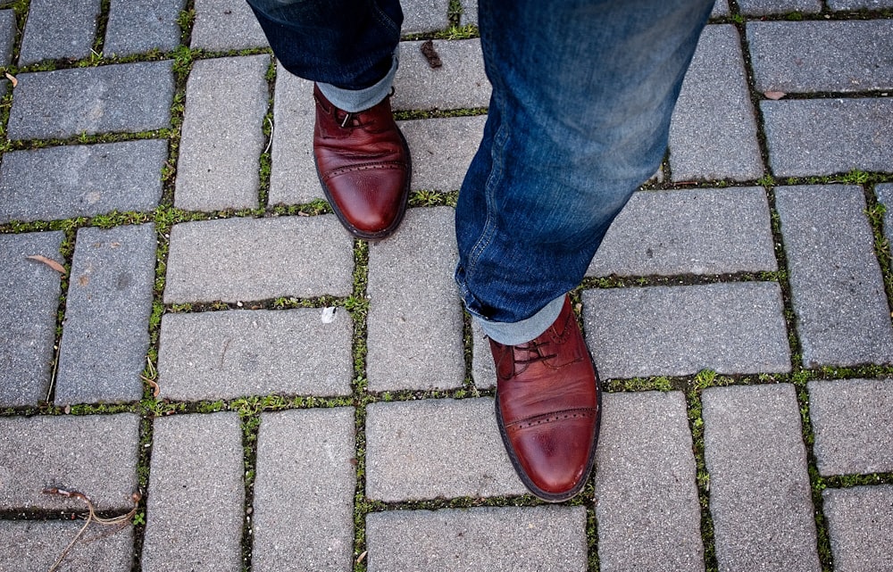 man wearing leather shoes walking on paved pathway