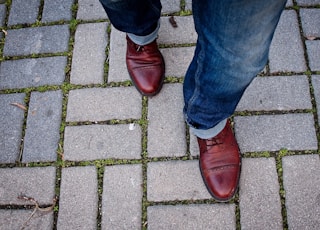 man wearing leather shoes walking on paved pathway