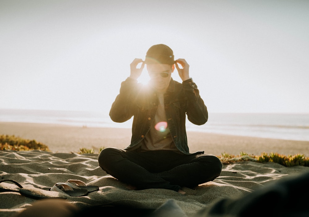 sitting man wearing black cap near body of water