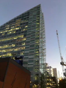 A sleek modern skyscraper under construction at dusk with golden lights glowing.
