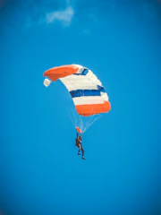 A vibrant aerial shot of a skydiver freefalling with a bright orange parachute against a clear blue sky.