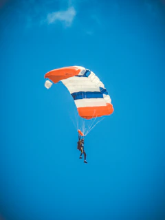 An action shot of a parachute opening mid-air against a bright blue sky, capturing the thrill of the jump.