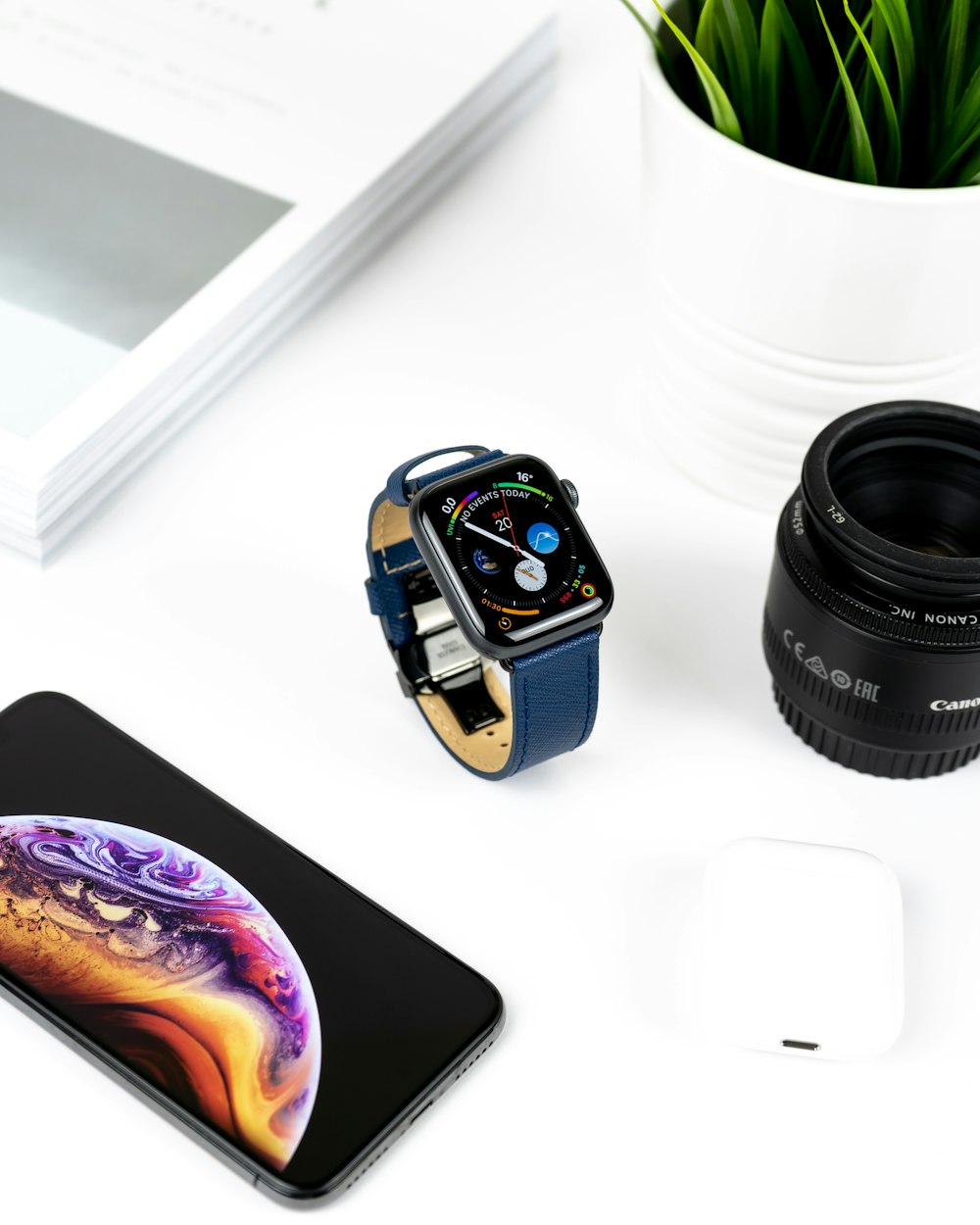 space grey aluminum case Apple Watch with blue leather band on table in between iPhone X and Canon zoom lens
