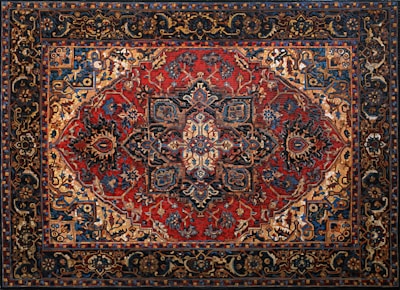 An intricately designed Persian rug featuring a central medallion with elaborate floral and geometric patterns. The color palette includes rich reds, deep blues, and earthy tones, with a detailed border surrounding the central motif.