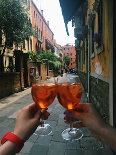 Friends clinking glasses with sunset orange and botanical green drinks, smiling warmly in the evening festival atmosphere.