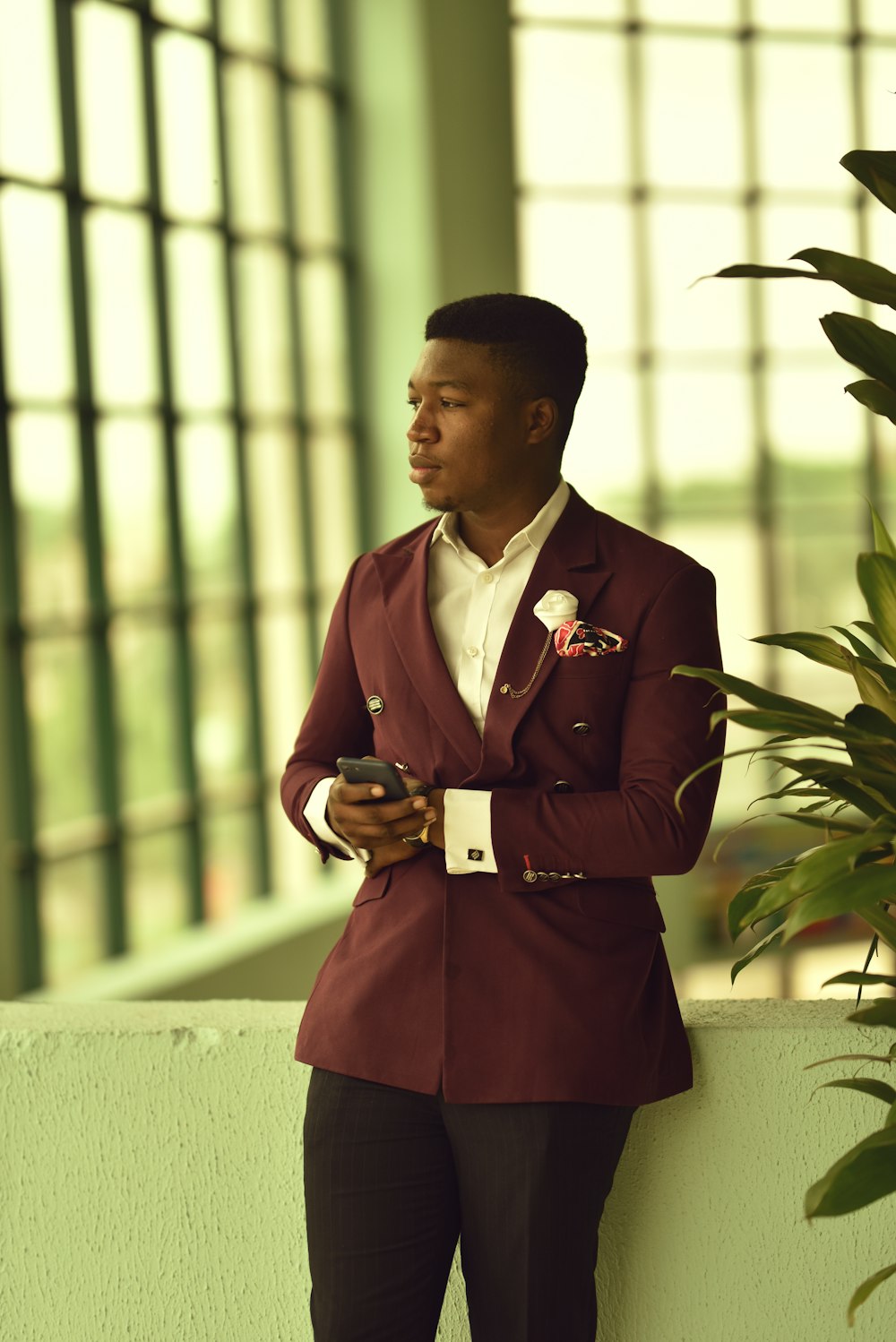 man in maroon peaked lapel suit jacket and blac dress pants leaning on white baluster