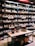 Shelves filled with various bottles of wine displayed in a store. The labels on the bottles and the signs above the shelves suggest a diverse selection. A table in the foreground exhibits additional bottles, and boxes are stacked below it with banners hanging down.