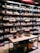Shelves filled with various bottles of wine displayed in a store. The labels on the bottles and the signs above the shelves suggest a diverse selection. A table in the foreground exhibits additional bottles, and boxes are stacked below it with banners hanging down.