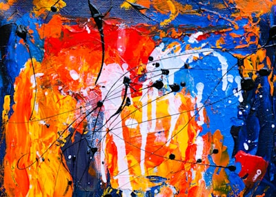 A vibrant abstract painting featuring bold strokes and splatters of color. Predominant hues include orange, red, and blue, with intertwined black lines adding movement and contrast. The texture is dynamic and expressive, showcasing layers of paint applied with energy and spontaneity.