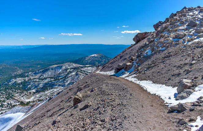 Runner crossing a rugged mountain trail with panoramic views of the Tarentaise and Aosta valleys under a clear sky.