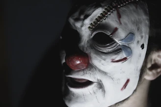 Close-up of a cracked porcelain clown mask with shadows creeping behind it.