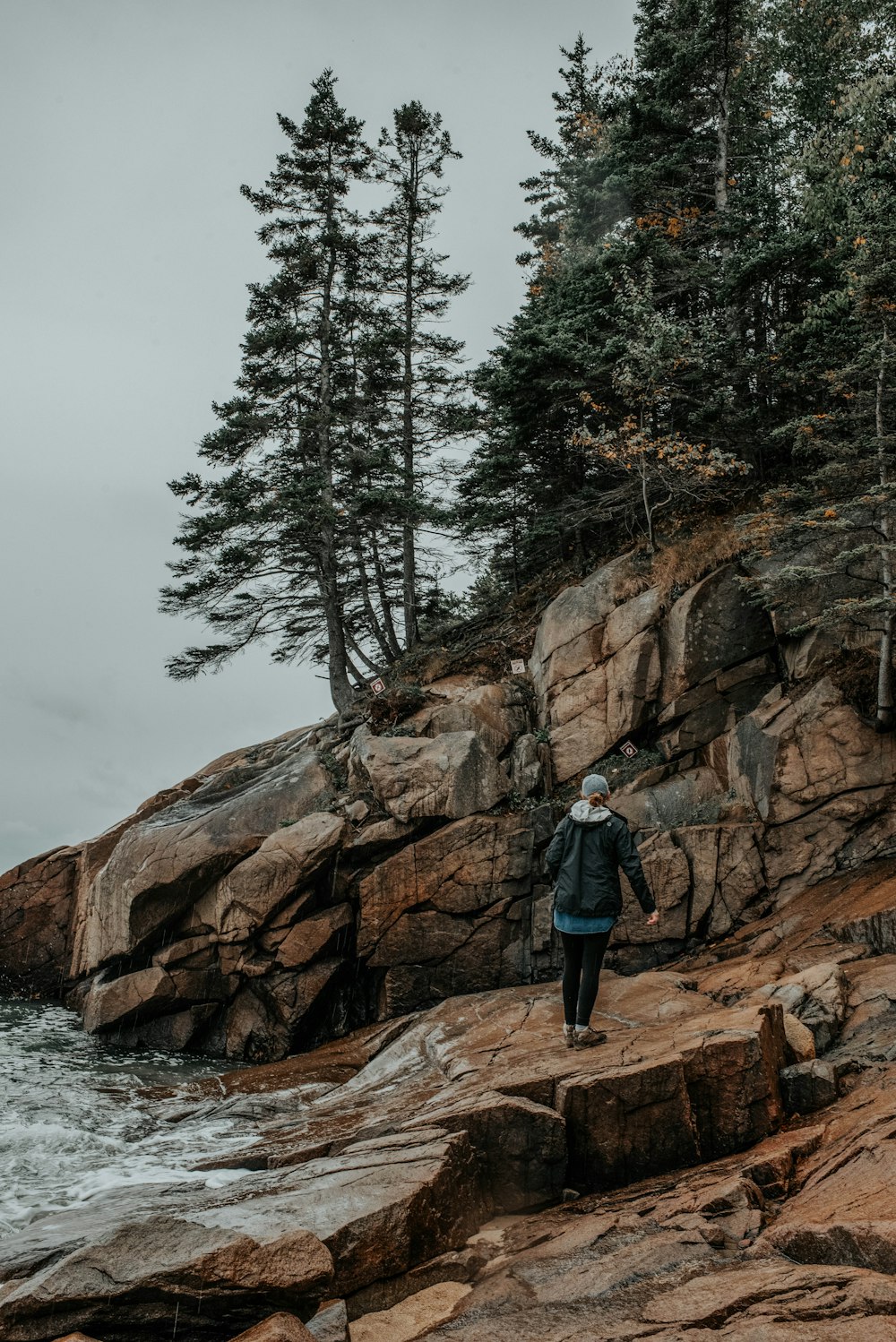 person stands on rock beside body of water