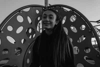 Photo of a young adult with metal braces smiling in a casual outdoor setting.