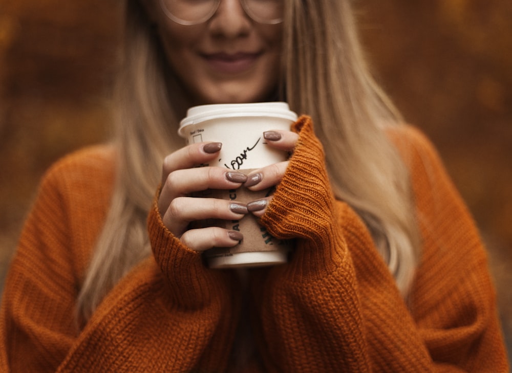smiling woman standing and holding coffee cup with lid